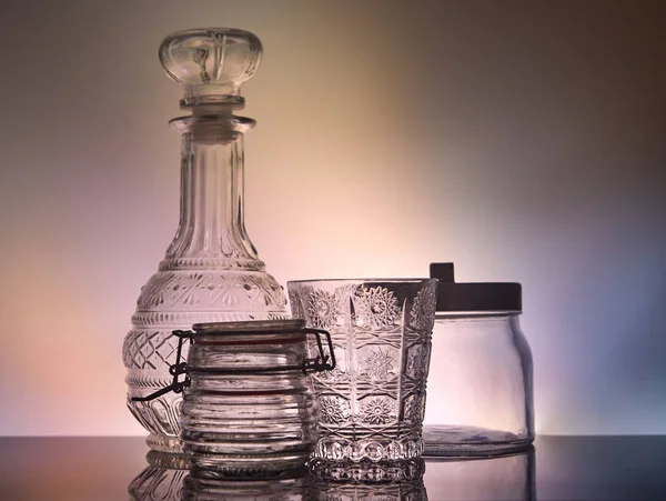 A decanter, a glass and glass jars standing on a stand with reflection with unusual lighting — Stock Photo, Image