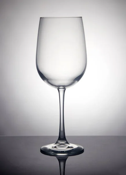 Una copa de vino sobre un fondo gris, de pie sobre un soporte negro con reflejo — Foto de Stock