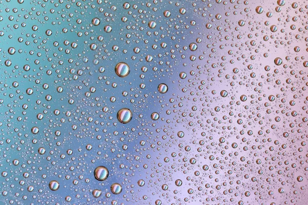 Gotas em vidro de diferentes tamanhos e cores em um fundo colorido, textura — Fotografia de Stock