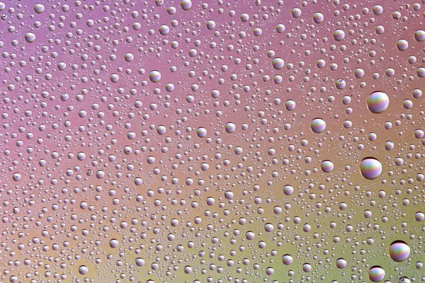 Gotas en vidrio de diferentes tamaños y colores sobre un fondo de color, textura — Foto de Stock