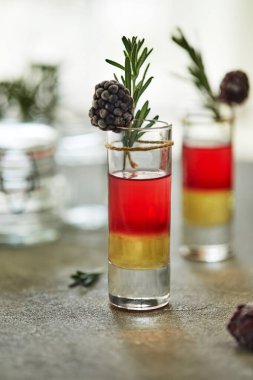 Ananas böğürtlenli kokteyl, bir garnitür dolusu donmuş böğürtlen ve gri-beyaz arka planda bir tutam biberiye.