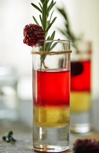 Pineapple blackberry cocktail in shots with a garnish of frozen blackberries and a sprig of rosemary on a gray-white background — Stock Photo, Image