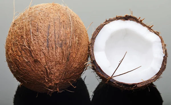 Coco inteiro e meio fresco em um fundo cinza com reflexão. Produto biológico vegano — Fotografia de Stock