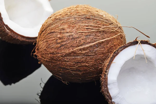 Coco fresco inteiro e cortado em duas metades em um fundo cinza com reflexão. Produto biológico vegano — Fotografia de Stock