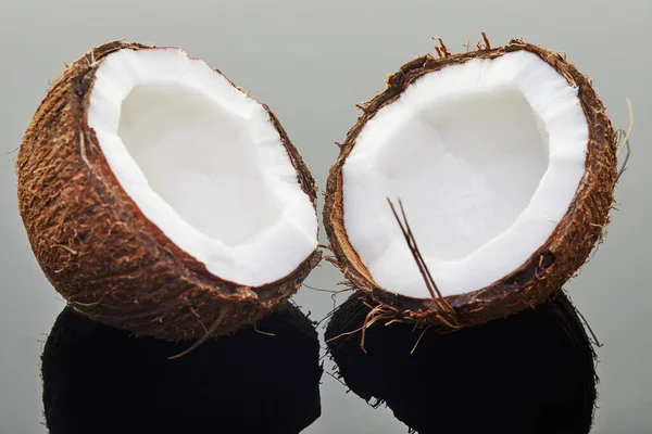Coco fresco cortado em duas metades em um fundo cinza com reflexão. Produto biológico vegano — Fotografia de Stock