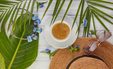 Mücevherlerle bezenmiş yaz. Kahve yaprakları palmiye şapkası bardakları ve beyaz ahşap arka planda boğucu olan bir yüzük..