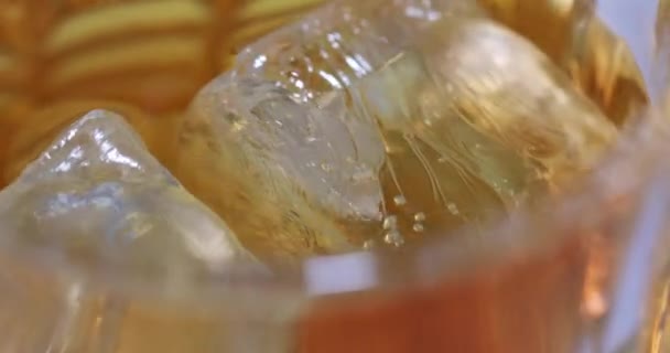 Un vaso de whisky o brandy con hielo, girando sobre un sustrato blanco. Vídeo macro — Vídeo de stock