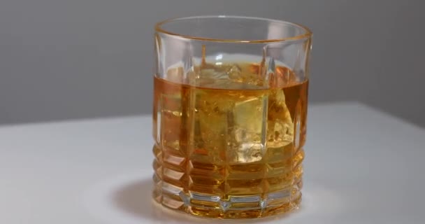 Un pahar de whisky sau coniac cu gheață, filându-se pe un substrat alb — Videoclip de stoc