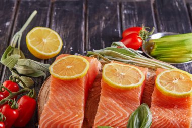 Çiğ somon filetosu dilimlenmiş, biberli limon biberiyesi ve ahşap bir masada kiraz domatesleri. Yan görünüm.