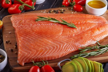 Çiğ somon fileto biber, limon biberiye ve kiraz domatesleri koyu ahşap bir masada..