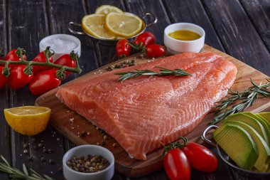 Çiğ somon fileto biber, limon biberiye ve kiraz domatesleri koyu ahşap bir masada..