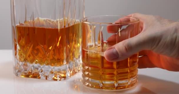 La main du mâle prend un verre de whisky ou de brandy avec de la glace et après une seconde met le verre vide en place — Video