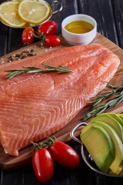 Çiğ somon fileto biber, limon biberiyesi ve kiraz domatesleri koyu ahşap bir masada. Yan görünüm