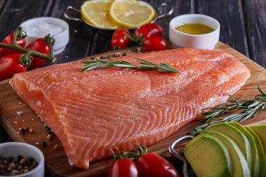 Çiğ somon fileto biber, limon biberiyesi ve kiraz domatesleri koyu ahşap bir masada. Yan görünüm