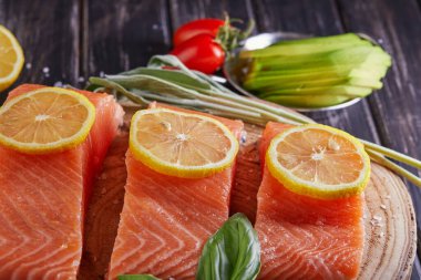 Çiğ somon filetosu dilimlenmiş, biberli limon biberiyesi ve ahşap bir masada kiraz domatesleri. Yan görünüm.