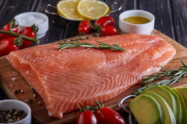 Çiğ somon fileto biber, limon biberiyesi ve kiraz domatesleri koyu ahşap bir masada. Yan görünüm
