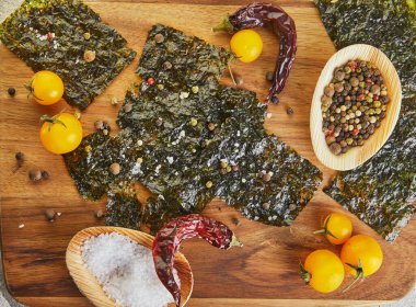 Çeri domatesli ve ahşap tahtada baharatlı çıtır Norveç yosunu. Japon yemeği nori. Kurutulmuş yosun çarşafları. Uzayı kopyala Düz yatıyordu