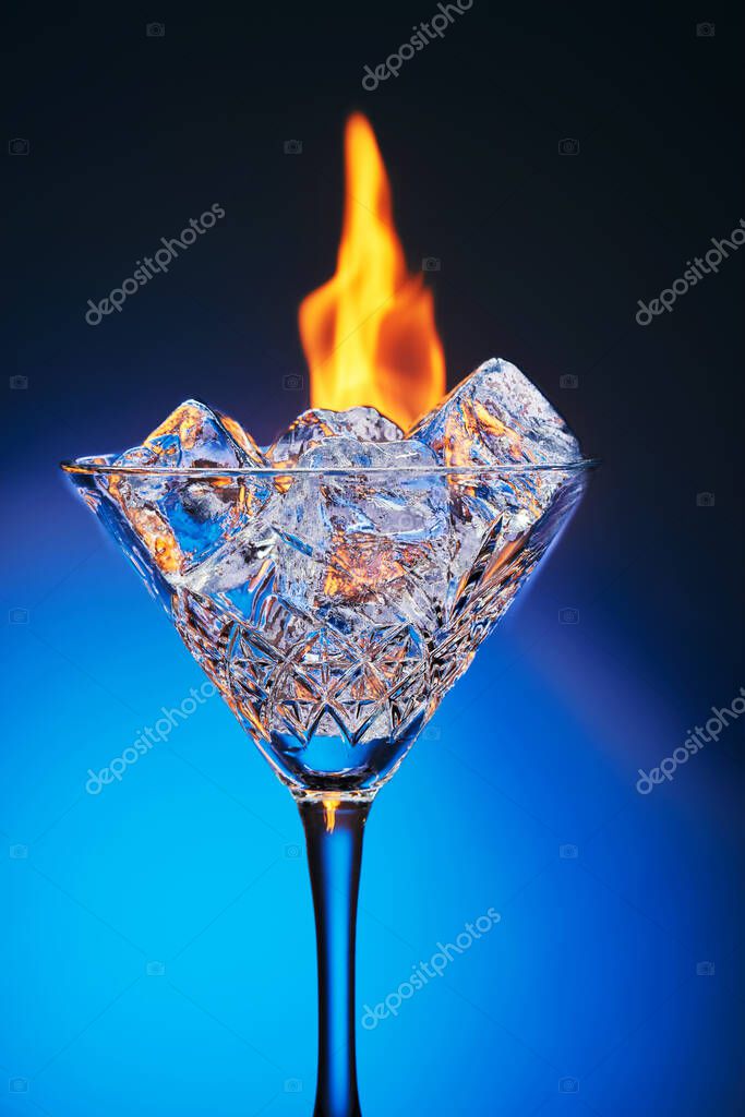 Hielo en un vaso de martini y fuego ardiente sobre un fondo azul con