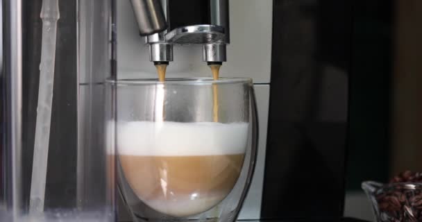 Verser le café d'une machine à café dans une tasse transparente avec du lait pour créer du café cappuccino — Video