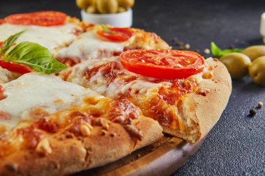 Siyah beton arka planda yemek pişirmek için İtalyan pizzası ve malzemeleri. Domates, zeytin, fesleğen ve baharat. Dilimlenmiş pizza üçgeni. Uzayı metin için kopyala. Yan görünüm
