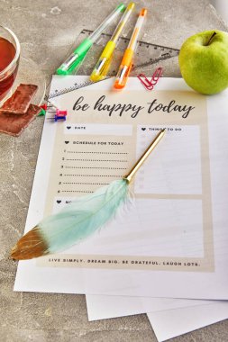 Renkli kalemler, üzerinde yazı olan günlük kağıtları ve gri beton arka planda bir elma..