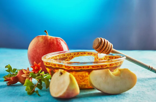 Rosh Hashanah, Yahudi Yeni Yıl tatili için bir kavramdır. Elma şeklindeki bir kasede çubuklar ve mavi arka planda nar yaprakları olan bal..