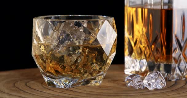 Błyszcząca szklanka whisky z kostkami lodu na drewnianej podstawce — Wideo stockowe