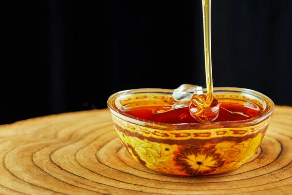 Rosh hashanah - jewish New Year holiday concept. A stream of honey flows into a bowl on a wooden stand.