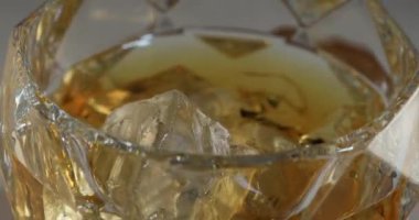 Yakın planda buz küplü dönen viski bardağı.
