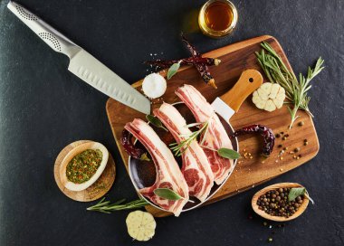 Pişirmek için malzemeli çiğ kuzu kaburga: Ahşap saplı bir tabakta tuz, biber, zeytinyağı ve otlar. Düz yatıyordu.