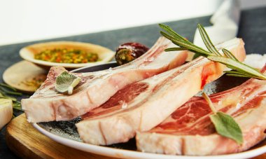 Pişirmek için malzemeli çiğ kuzu kaburga: Ahşap saplı bir tabakta tuz, biber, zeytinyağı ve otlar. Kapat.