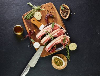 Pişirmek için malzemeli çiğ kuzu kaburga: Ahşap saplı bir tabakta tuz, biber, zeytinyağı ve otlar. Düz yatıyordu.