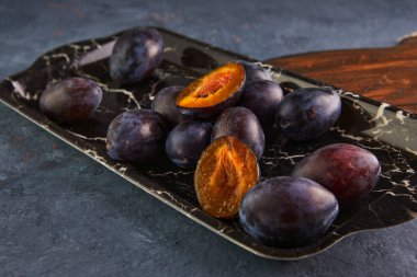 Mor bir arka planda mermer tepside erik dolu bir hayat.