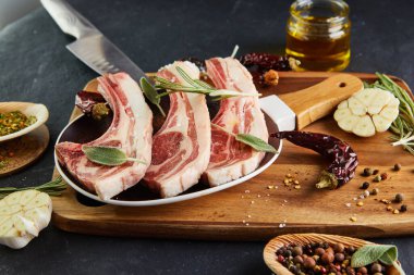 Pişirmek için malzemeli çiğ kuzu kaburga: Ahşap saplı bir tabakta tuz, biber, zeytin yağı ve otlar..