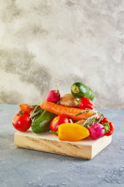 Ahşap bir podyumda, mavi-gri arka planda çeşitli sebze ve meyveler yatıyor. Metin için alanı kopyala.