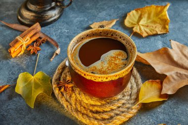 Sonbahar, sonbahar yaprakları, sıcak bir fincan kahve ve mavi bir masanın arka planında sıcak bir eşarp. Mevsimlik, sabah kahvesi, pazar rahatlaması ve hayat konsepti. Kapat.