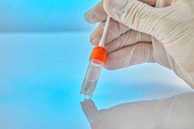 DNA testi. DNA analizi için sıvı test tüpü ve mavi arka planda yansıması olan bir çubuğu tutan eldivenli bir el..