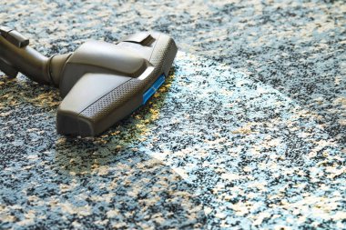 Kapalı alanda elektrikli süpürgeyle halıdaki kiri temizliyorum..