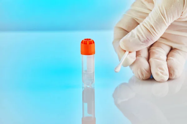 DNA test. Test tube with liquid for DNA analysis and a gloved hand holding a stick on a blue background with reflection.