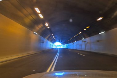 Bir araba aydınlık bir tünelden geçer, gün ışığına doğru, yansımalar, simetri, ve zıt sıcak ve serin ışık tonlarıyla.