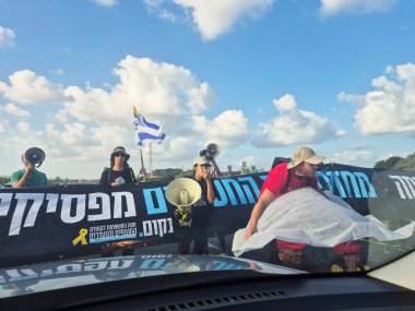 Zichron Yaakov, İsrail - 26 Ağustos 2025: Megafonlu ve bayraklı protestocular, işaretler ve müzik aletleriyle siyasi mesajlar vererek parlak gökyüzü altındaki yolu kapattılar.