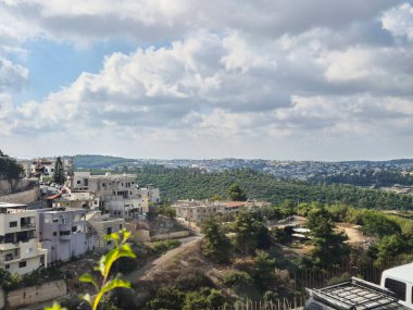 Tamamlanmamış yapıları olan modern yamaçlardaki evler yemyeşil ve bulutlu bir gökyüzünün altındaki uzak şehir manzarasına bakıyor..