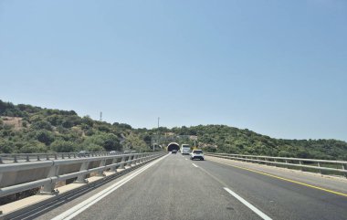 Zichron Yaakov, İsrail - 15 Ağustos 2025: Açık otoyol, açık bir gökyüzü altında ağaçlar ve kırsal yerleşimlerle çevrili araçlarla ilerliyor.