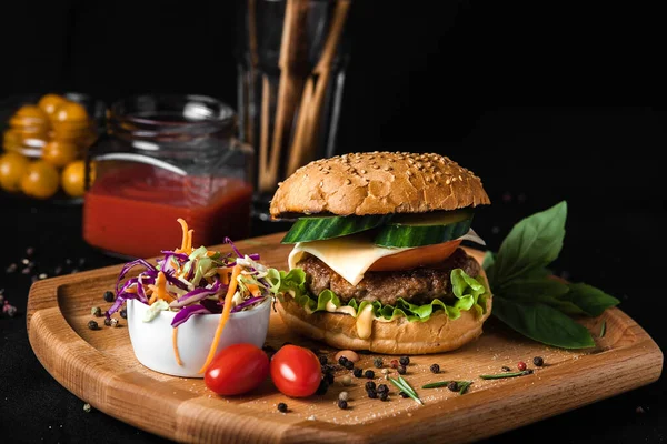 Meat burger with on wooden Board for take away with cabbage salad, vegetables and cheese. On black background.