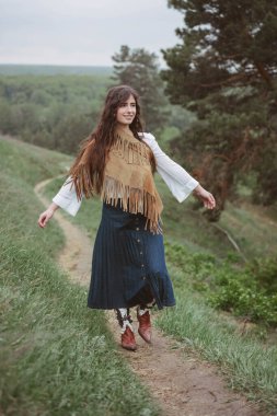 Voronezh, Rusya, Mayıs 2017. Kıyafet modası. Kız doğada iz sürüyor. Uzun pileli kot etek, kovboy çizmesi, süet kahverengi pelerin giymişti. Sadece editör kullanımı.