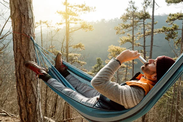 Man relaxing lying and drinking in hammock on top of mountain. — Stock Photo, Image