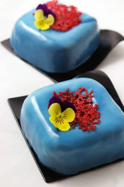 Blue desserts on black coasters with pansies and red lace crepe decoration