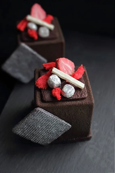 Dark chocolate textured cube dessert with strawberry, silver cookie decorations and red sponge top view