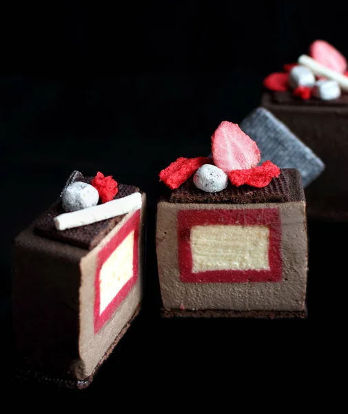 Sliced dark chocolate textured cube dessert with strawberry and vanilla insertion, silver cookie decorations and red sponge