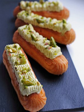 Siyah plaka üzerinde şekerli antep fıstığı ile Antep fıstığı eclairs